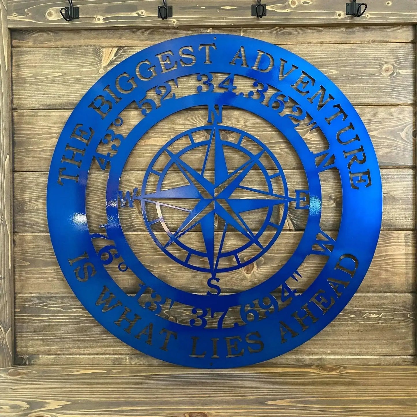 The Biggest Adventure Compass With Personalized GPS Coordinates Metal Sign, showcasing a blue compass design on wood, symbolizes exploration, perfect for indoor or outdoor decor and meaningful personalization.