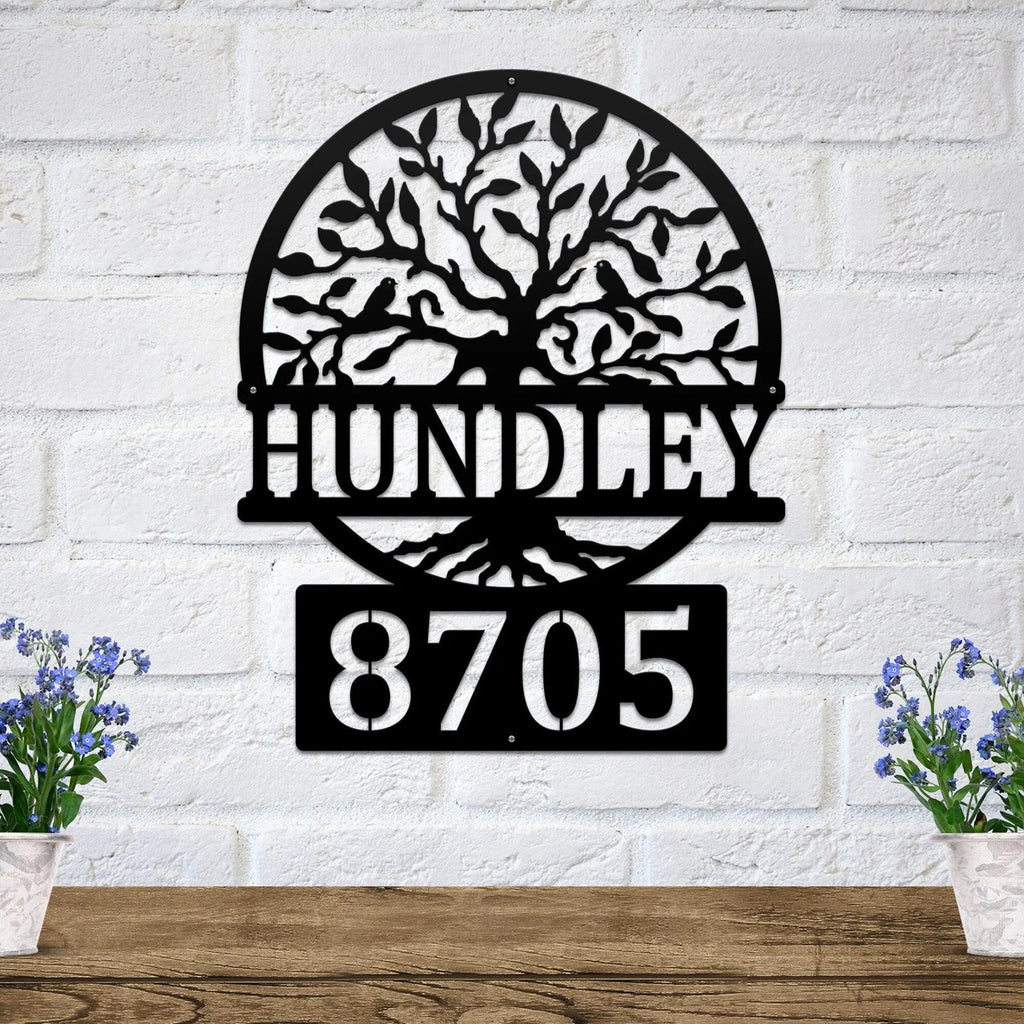 Decorative metal wall art with tree design and house numbers "HUNDLEY 8705" on white brick wall, custom outdoor address plaque, modern home exterior décor