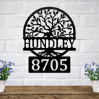 Decorative metal wall art with tree design and house numbers "HUNDLEY 8705" on white brick wall, custom outdoor address plaque, modern home exterior décor