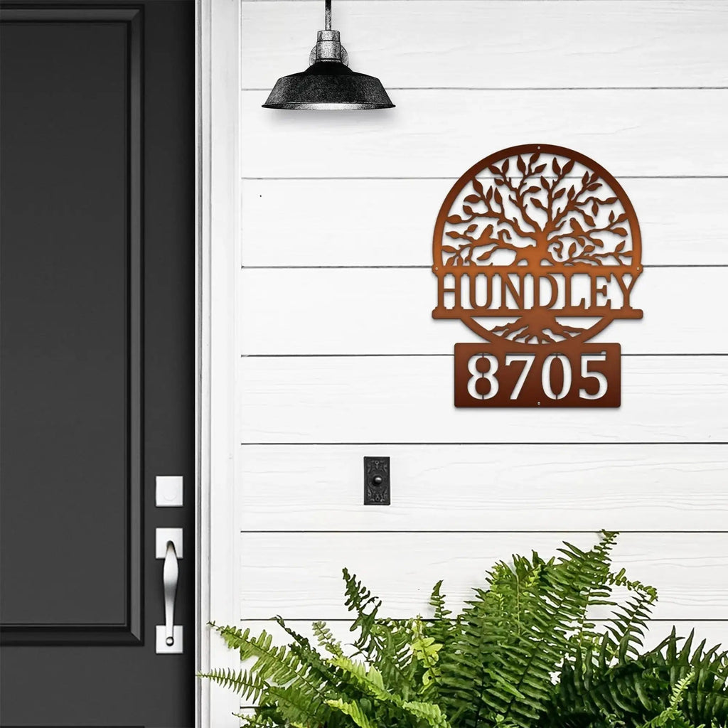 Decorative metal house number sign with tree design on white wall next to black door, custom outdoor address plaque, modern home exterior décor