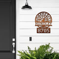Decorative metal house number sign with tree design on white wall next to black door, custom outdoor address plaque, modern home exterior décor