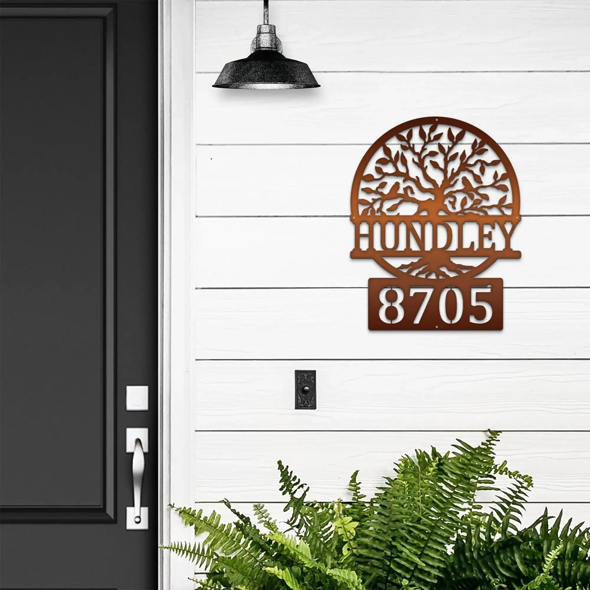 Decorative metal house number sign with tree design on white wall next to black door, custom outdoor address plaque, modern home exterior décor