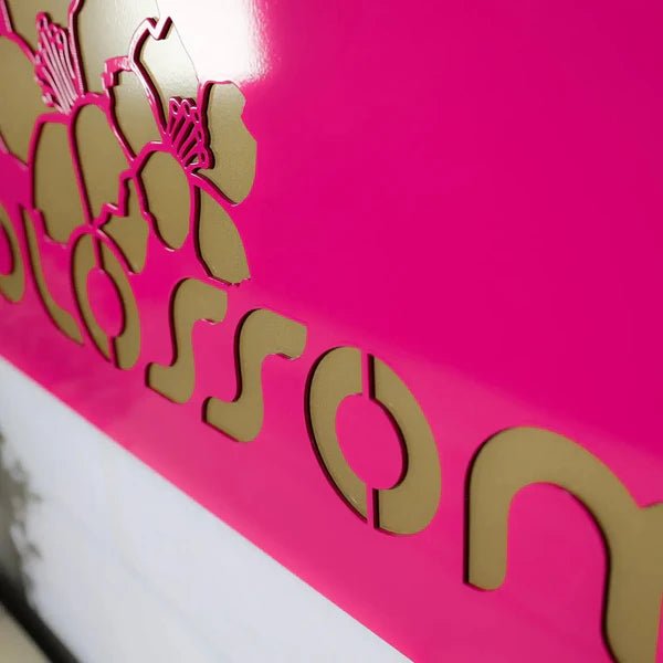 Close-up of a pink metal product featuring gold floral designs and text, highlighting intricate detailing and elegant craftsmanship.