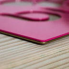 Pink metal sign placed on a wooden surface, showcasing smooth texture and decorative design.
