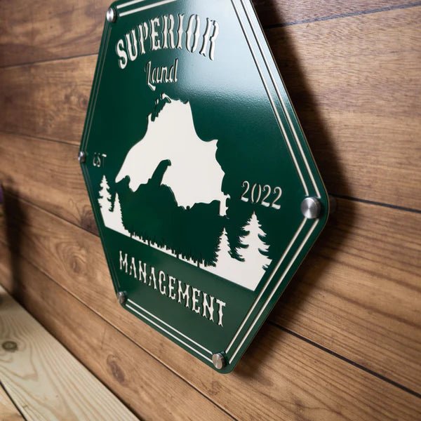Hexagonal metal sign featuring “Superior Land Management” with a mountain design, displayed on a wooden background, showcasing rustic, outdoor-inspired branding and durable metal construction.