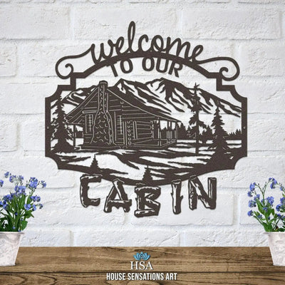 Rustic “Welcome to Our Cabin” metal sign with cabin illustration on white brick wall, custom powder coated wall décor, farmhouse entry welcome sign design