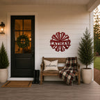 Red customized windmill metal wall art with "Latham est 2021" mounted on a white farmhouse porch wall above a wooden bench with a "welcome" pillow and plaid blanket.