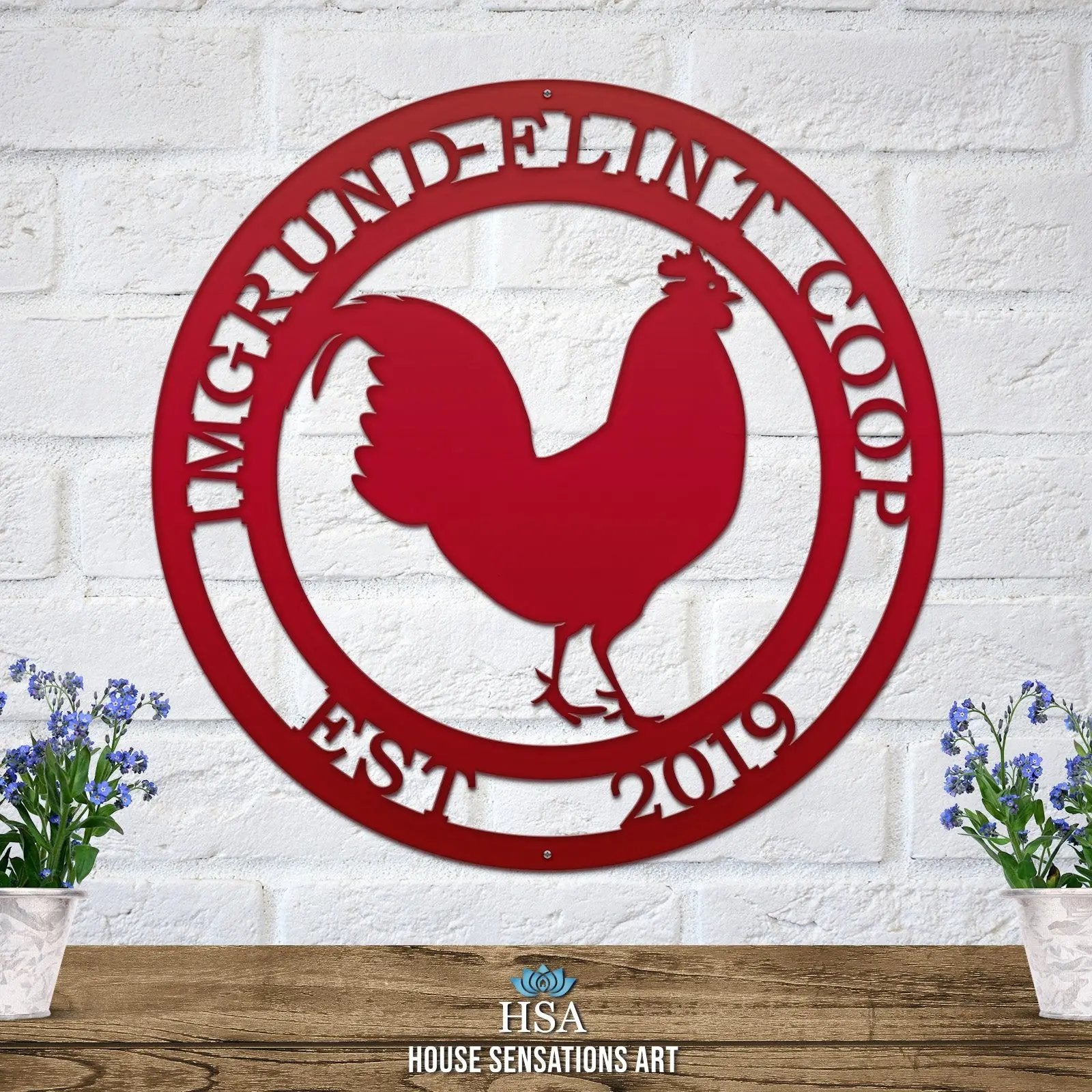 Deep red circular ranch metal sign with cut-out rooster and “IMGRUND-FLINT COOP EST. 2019” text on brick wall.