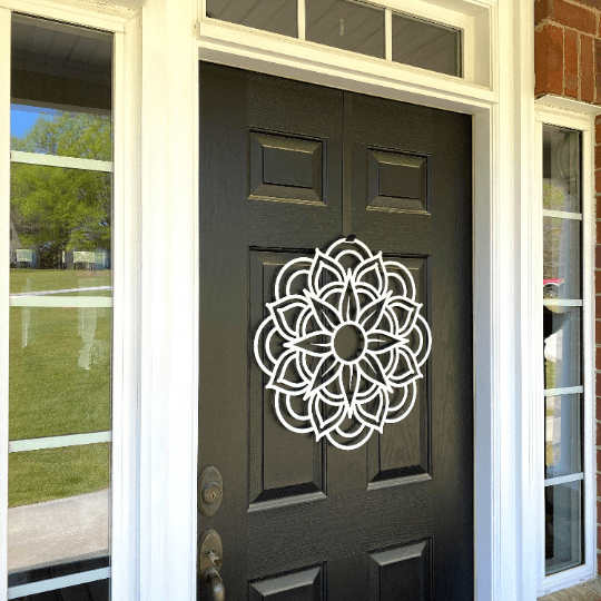 White mandala metal flower wreath on black door with glass panels, modern floral decor, handcrafted outdoor metal sign, elegant entryway design