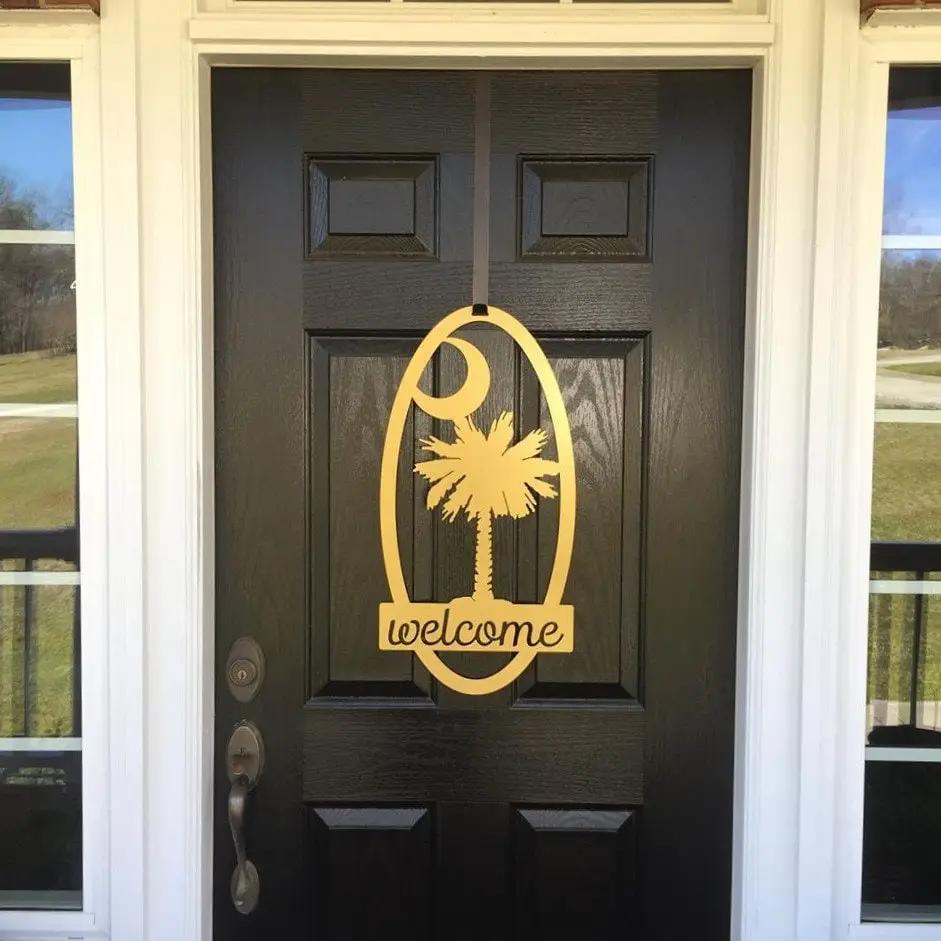 Decorative metal “Welcome” sign with palm tree design hanging on black door, custom outdoor home entrance décor