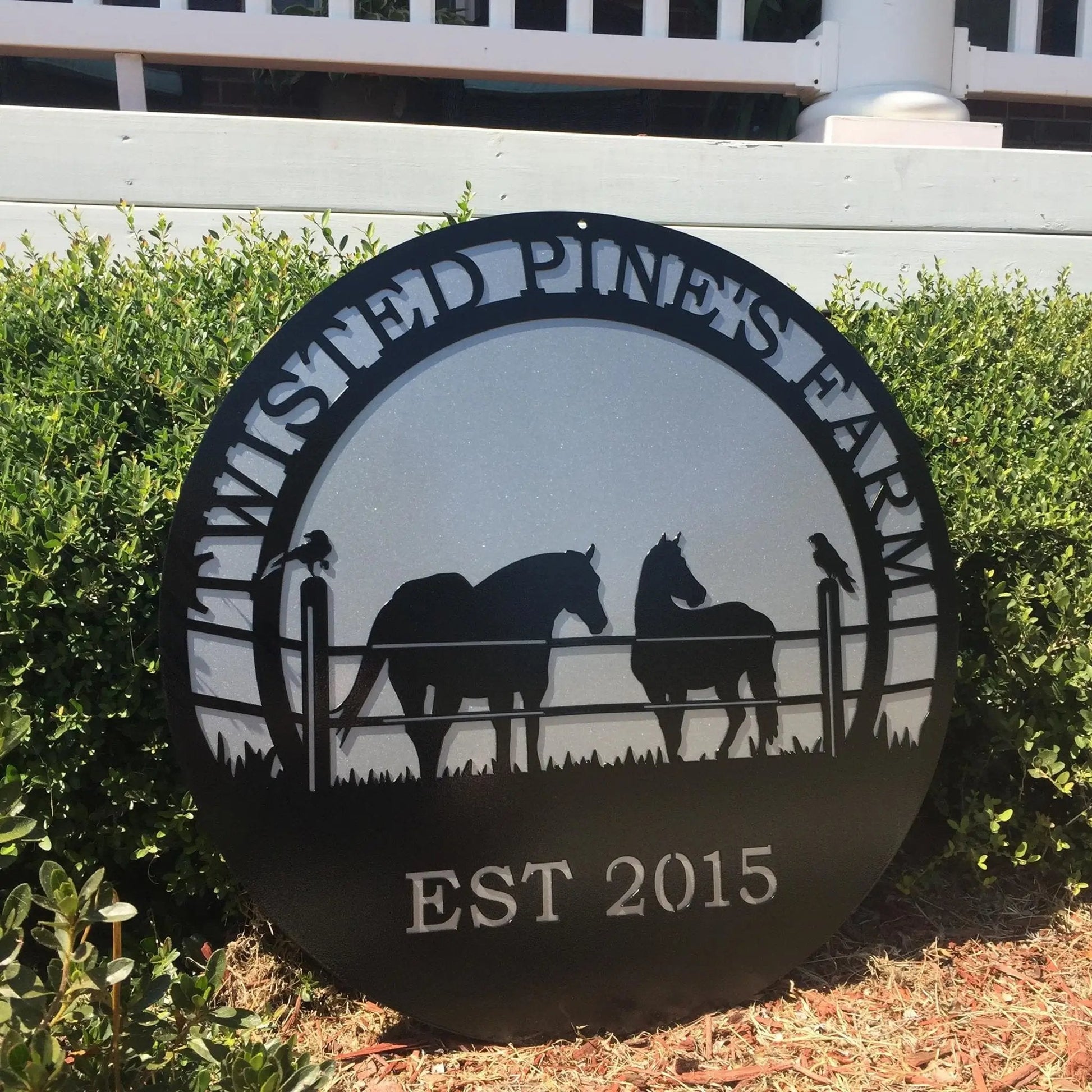 Angled view of black custom laser cut metal ranch sign showing horses in pasture, with “TWISTED PINE’S FARM EST 2015” text.
