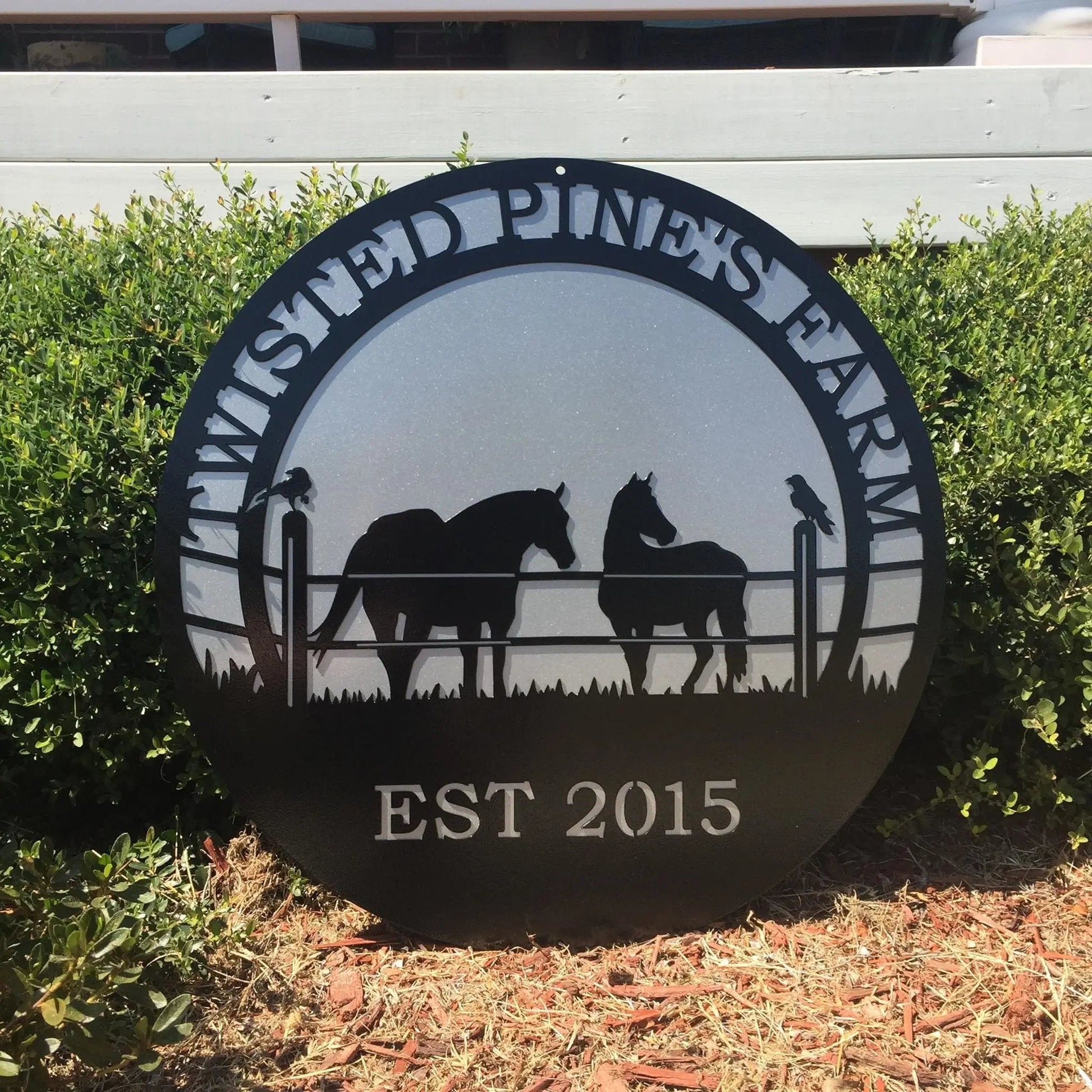 A black custom laser cut metal ranch sign showing horses in pasture, with “TWISTED PINE’S FARM EST 2015” text, placed outdoors.