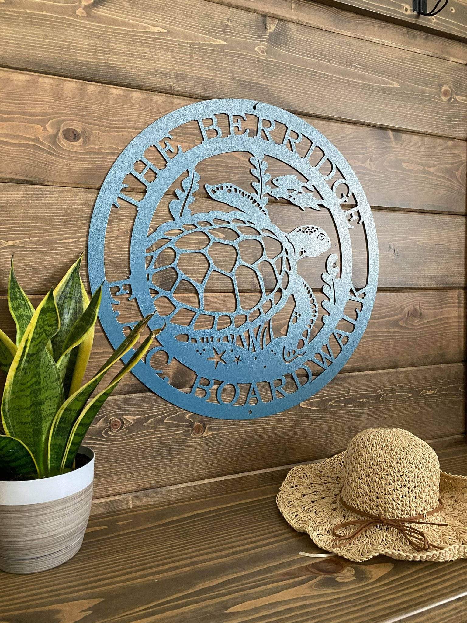 Side view of textured blue custom laser cut metal sign showing turtle, seaweed, and fish, with “THE BERRIDGE E.A.C BOARDWALK” text, mounted on wood wall.