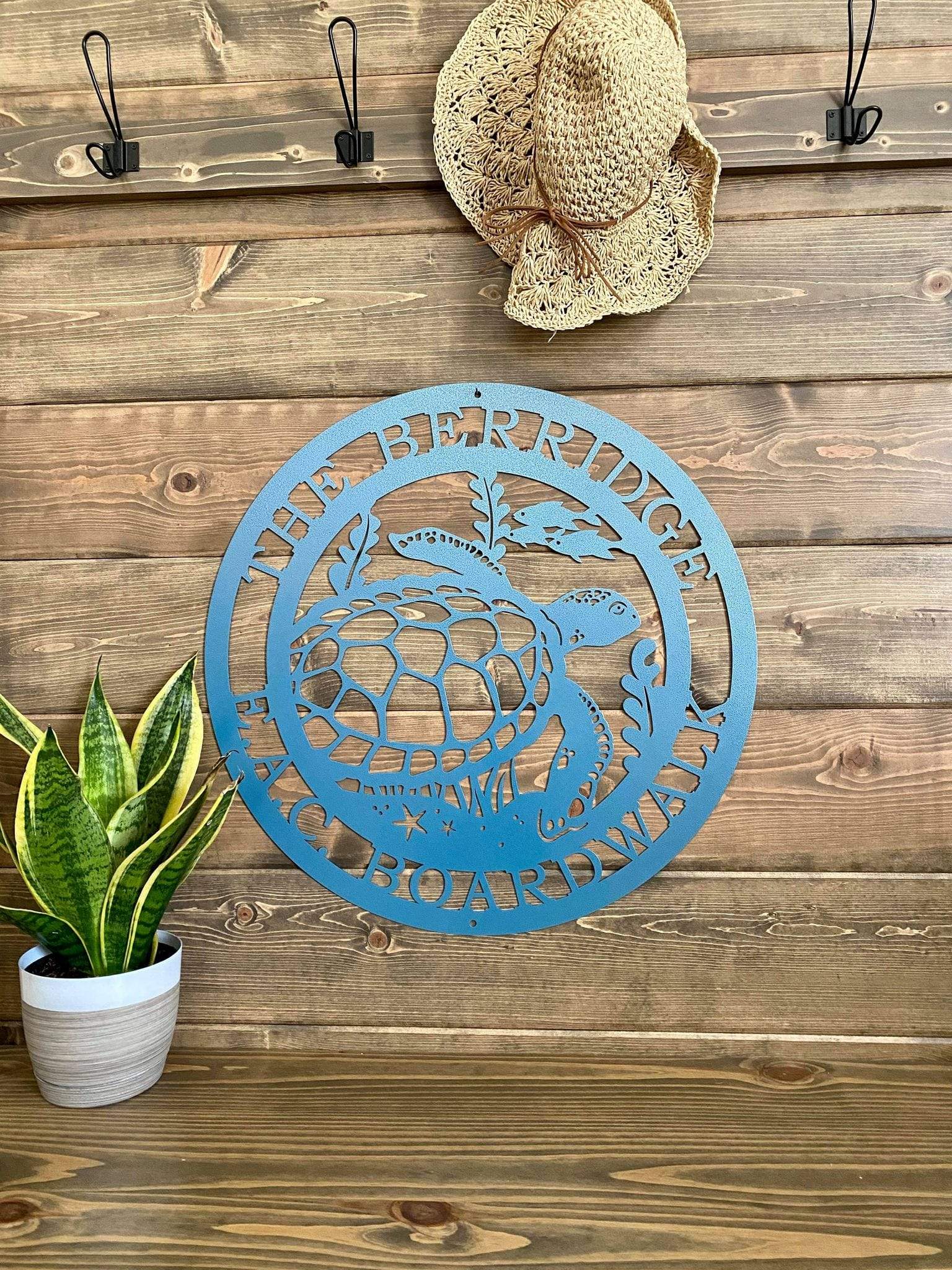 Textured blue custom laser cut metal sign showing turtle, seaweed, and fish, with “THE BERRIDGE E.A.C BOARDWALK” text, mounted on wood wall.