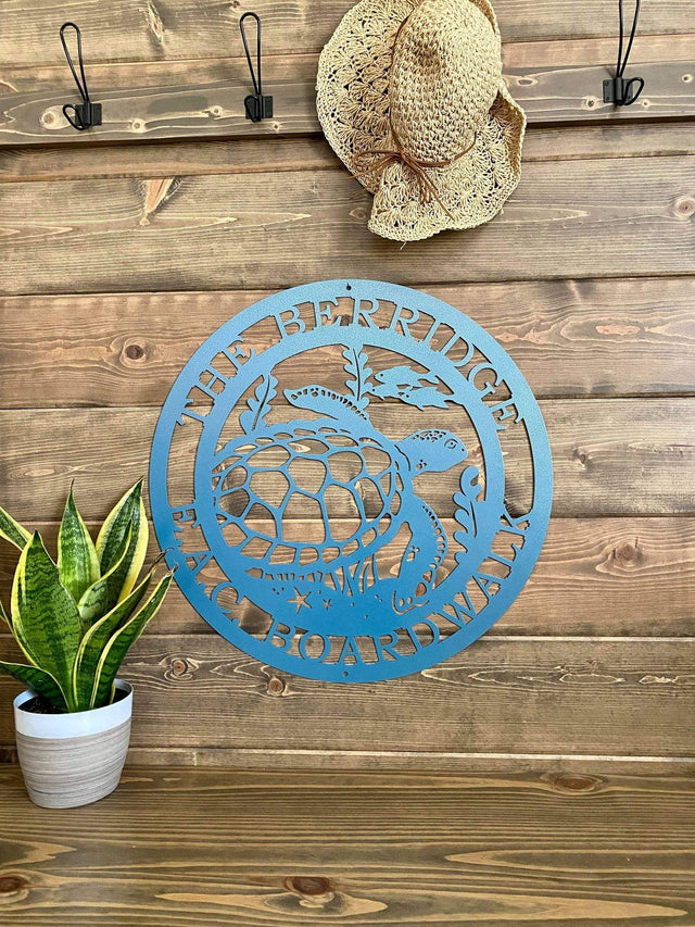 Textured blue custom laser cut metal sign showing turtle, seaweed, and fish, with “THE BERRIDGE E.A.C BOARDWALK” text, mounted on wood wall.