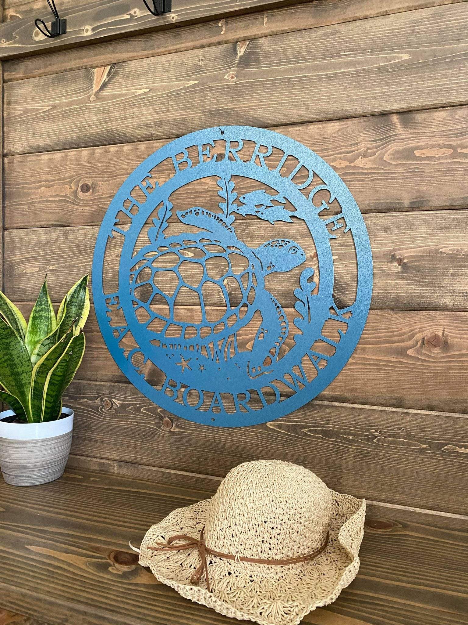 Angled view of textured blue custom laser cut metal sign showing turtle, seaweed, and fish, with “THE BERRIDGE E.A.C BOARDWALK” text, mounted on wood wall.