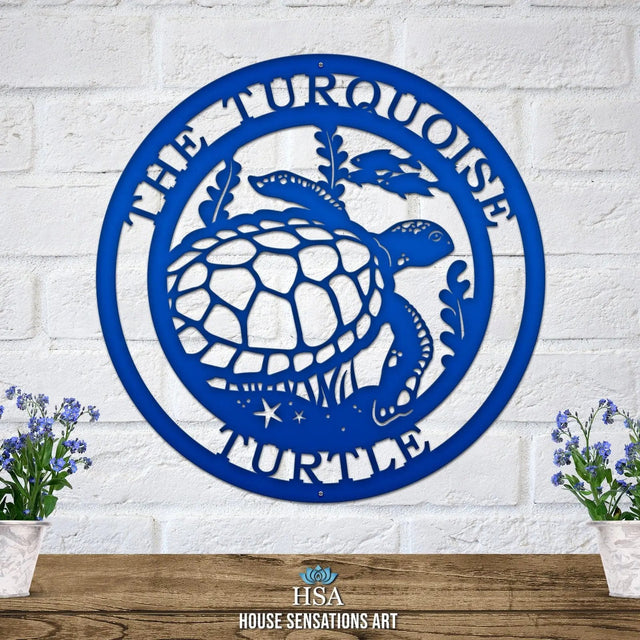 Bright blue custom laser cut metal sign showing turtle, seaweed, and fish, with “THE TURQUOISE TURTLE” text, mounted on a brick wall.