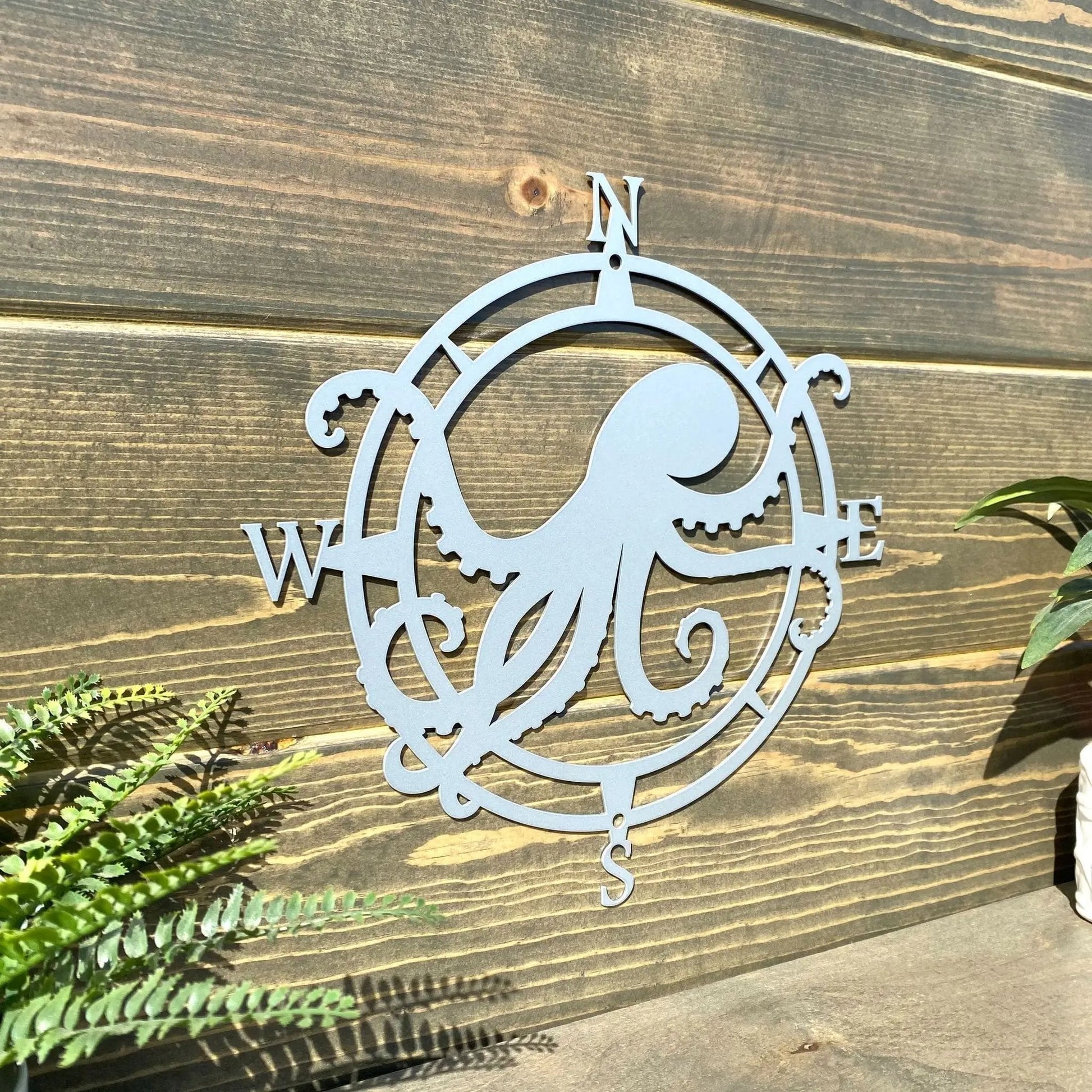 Polished chrome compass design metal sign, octopus centered with arms W and E, mounted for seaside-style front decor.
