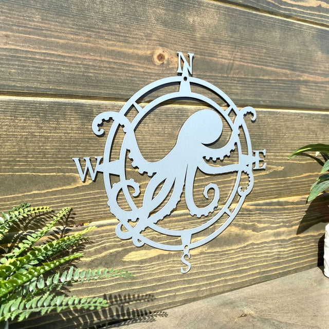 Polished chrome compass design metal sign, octopus centered with arms W and E, mounted for seaside-style front decor.