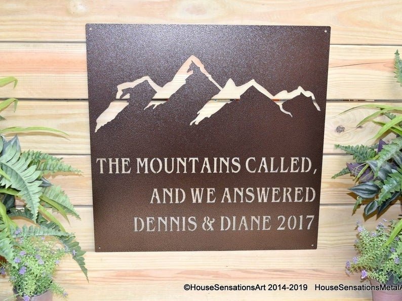 Decorative metal sign featuring a mountain design and custom text, displayed on a wooden background, showcasing rustic style, detailed craftsmanship, and durable metal construction.