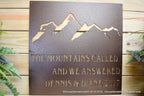 Metal sign featuring a mountain design with engraved text, displayed on a wooden background, highlighting rustic style, detailed craftsmanship, and durable construction.