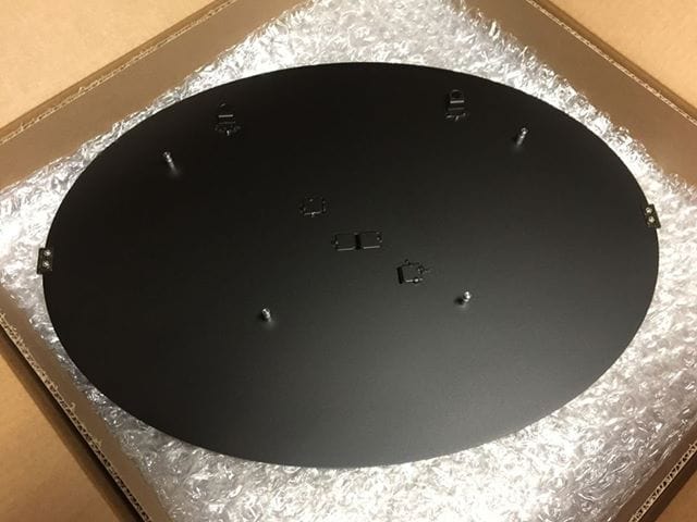 HouseSensationsArt Black circular Weld Mount System on bubble-wrapped surface with cardboard edges, featuring strong adhesive fasteners for any surface, custom powder-coated metal sign, durable outdoor-ready mounting, modern matte black finish, easy installation, personalized metal décor